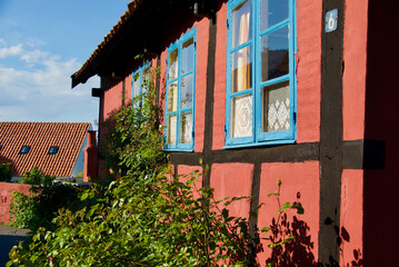 Wall Mural - Exterior of a red half-timbered building with windows with blue frames and a lush inner garden. 