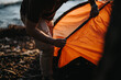 A close-up view of friends working together to set up an orange tent near a lake, enjoying their outdoor leisure time.