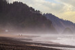 Couple walking along a misty beach on a beautiful colorful morning. Oregon beach walking at dawn on a springtime day with a rugged coastline in the background.
