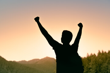 Adventurous man in forest mountain sunrise looking up to the sky with fist up, never give up, people power, perseverance, resilience 