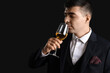 Young sommelier with glass of wine on black background, closeup