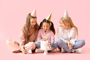 Wall Mural - Cute little girls in party hats with Birthday cake sitting on pink background