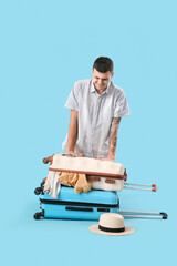 Sticker - Young male tourist trying to close suitcase full of clothes on blue background