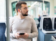 Relaxed young bearded man using his smartphone during trip in public transport ..