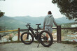 © Taras Grebinets - Rear view of a young active man cyclist standing near his electric battery powered bike, admiring beautiful mountains, enjoying riding in the nature