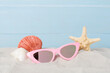 Sunglasses with summer decor on sand against wooden background