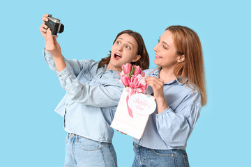 Canvas Print - Beautiful mature woman with bouquet of tulips and her daughter taking selfie on blue background. Mother's Day celebration