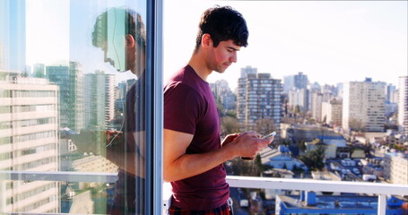 Wall Mural - man in purple shirt standing on balcony using smartphone, cityscape in background