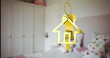 A golden house-shaped keychain hanging in focus with blurred bedroom background