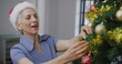Caucasian senior woman with gray hair is decorating Christmas tree
