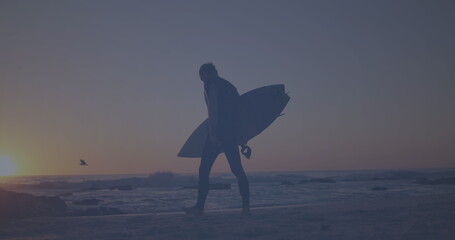 Wall Mural - Caucasian young adult walking on beach, holding surfboard