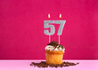 Birthday celebration with candle number 57 - Chocolate cupcake on pink background