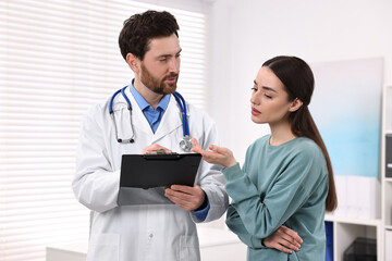 Wall Mural - Doctor with clipboard consulting patient during appointment in clinic