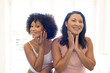 Biracial mother and adult daughter are standing, touching faces, smiling at home, copy space
