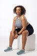Biracial young female plus size model wearing sportswear sitting on white block, on white background
