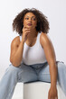 Biracial young female plus size model sitting, touching chin, looking thoughtful on white background