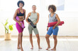 © Wavebreak Media - Three diverse women holding yoga mats, standing together in studio, smiling