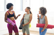 © Wavebreak Media - Three diverse women are chatting in a bright yoga studio, holding mats