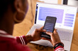 © Wavebreak Media - African American young woman indoors with phone, laptop showing AI Chat Bot Screen at home
