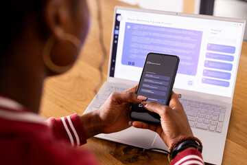 African American young woman indoors with phone, laptop showing AI Chat Bot Screen at home