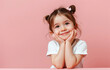 Cute little girl smiling and looking up, holding her chin with both hands on pink background