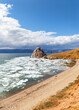 Spring on Baikal Lake. View of natural landmark - Shamanka Rock during ice drift on sunny May day. Sandy deserted beach on coast of Olkhon Island awaits tourists. Scenic landscape. Spring travels