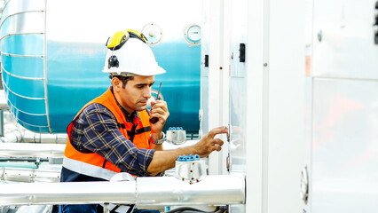 Male technical foreman in safety uniform inspects maintenance work talking on radio call with colleague with to look at plumbing and electrical systems on the roof of a building