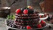 A stack of chocolate pancakes drizzled with maple syrup and fresh berries