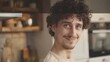 Close up of a young handsome positive curly man with blue eyes with a smiling face wearing casual beige tshirt looking at camera and standing alone in morning in the modern kitchen at  : Generative AI