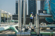 Focused engineer in hard hat and reflective vest standing amidst rooftop mechanical structures, consulting blueprints.