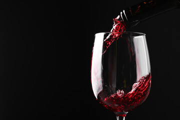 Sticker - Pouring red wine into glass against black background, closeup. Space for text