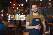 Portrait of Owner / Waiter at Restaurant. Portrait of handsome young male coffee shop owner standing at cafe. Portrait of a handsome barista in t-shirt and apron