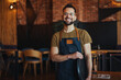 Happy confident young waiter entrepreneur looking at camera, smiling male small cafe business owner employee standing in restaurant, millennial businessman wear apron posing in coffee shop