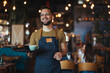 Waist up portrait of handsome waiter smiling cheerfully at camera standing in restaurant or cafe, copy space. Young waiter serving coffee in a cafe and looking at camera.