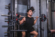 © Mdv Edwards - Dedicated and focused young male athlete doing back squats on a smith machine in a well-equipped gym, showing strength and concentration.