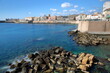 The Eastern rocky coast of Ortigia Island, Syracuse, Sicily, Italy, with clear and colorful water and Castello Maniace (Maniace castle) in the background on the left