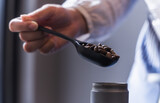Fototapeta Natura - Close up barista holding black roasted coffee in spoon preparing to make coffee in shop