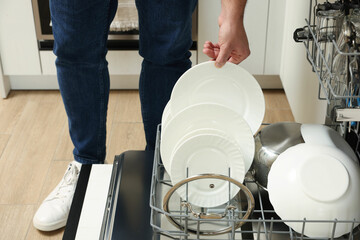 Canvas Print - Man loading dishwasher with plates indoors, closeup