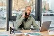 © Bliss - black man sits at a desk, fully engaged on a cell phone call, deep in conversation.