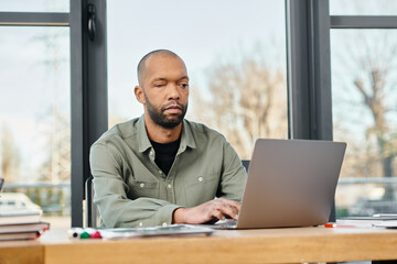 A man with myasthenia gravis sitting at a desk, focused on his laptop screen, working on a project in a modern office setting.