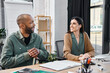 © Bliss - disabled man and a woman engage in a discussion while seated at a table in a corporate office setting.