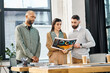 © Bliss - A diverse group of professionals stand around a table, engrossed in a magazine, brainstorming ideas for a project in an office setting.