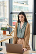 © Bliss - A woman standing in front of a laptop computer in an office setting, focused and engaged in her work.