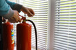 hand presses the trigger fire extinguisher available in fire emergencies conflagration damage background. Safety