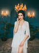 Fantasy woman dark curly elegant hair bun hairstyle. Sexy beauty face red pink make-up girl in luxury room crystal chandelier shines. Long vintage white dress silk peignoir pearl set beads art style 