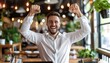 Young businessman celebrating success in front of laptop with arms raised in joy