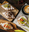 Freshly baked croissants with berries jam, chocolate and fruits with a cup of cappuccino. Dark wooden background. 