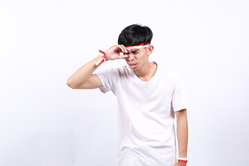 Frustrated asian young boy with red white ribbon for celebrating Indonesia independence day standing while holding head