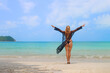 Carefree tan woman stand on the beach with outstretched hands and feel happiness. Breeze wave her pareo. Relaxation concept. Background with copyspace.