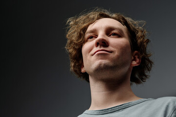 Wall Mural - Low angle closeup studio portrait of self-confident young Caucasian man with curly hair smirking, copy space